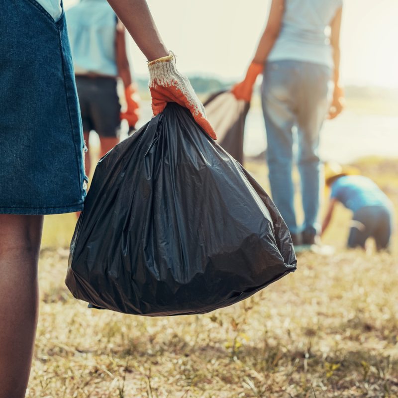 woman hand picking up garbage and hand holding black bag at park